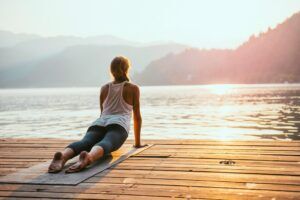 woman practicing yoga poses outdoors, with the sun setting in the horizon practicing self care