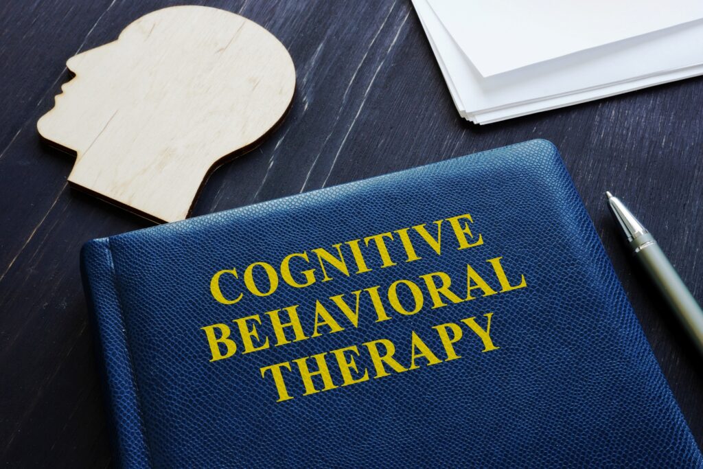 Cognitive behavioral therapy CBT book and wooden head shape.